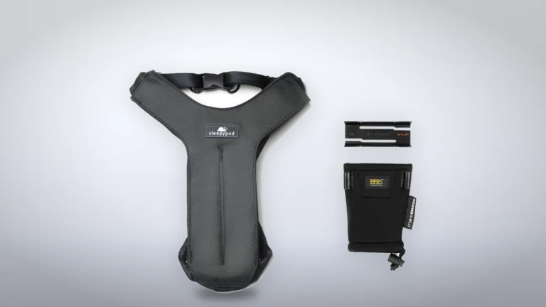 Charcoal Grey Clickit Sport harness laid flat beside its S-Clip and Buckle Shield on a light gray backdrop